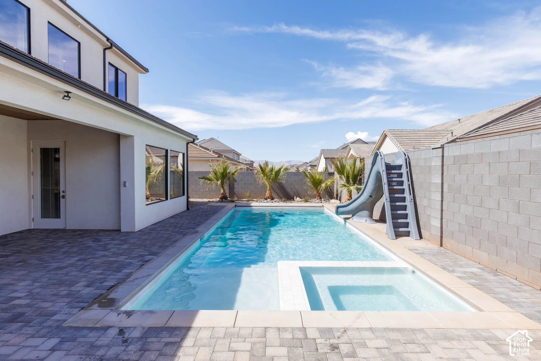 Resort-style backyard oasis featuring a resort-style swimming pool with integrated spa, travertine-look paved decking, a water slide, and mature tropical landscaping
