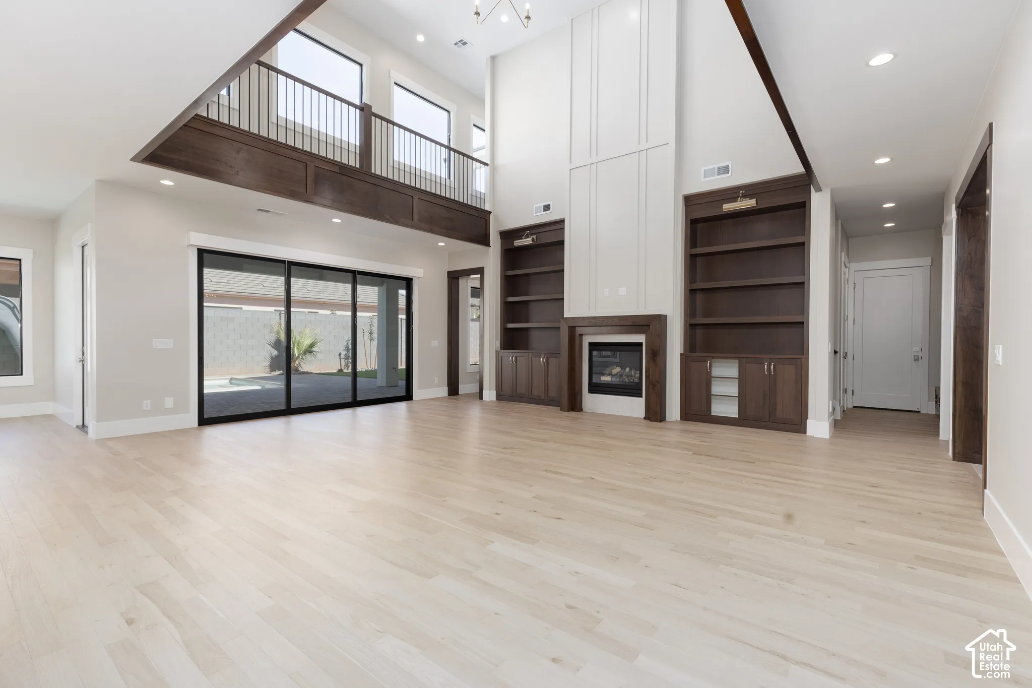 Two-story ceiling, light wood-finish flooring, built-in shelving, fireplace with mantel, and large sliding glass doors