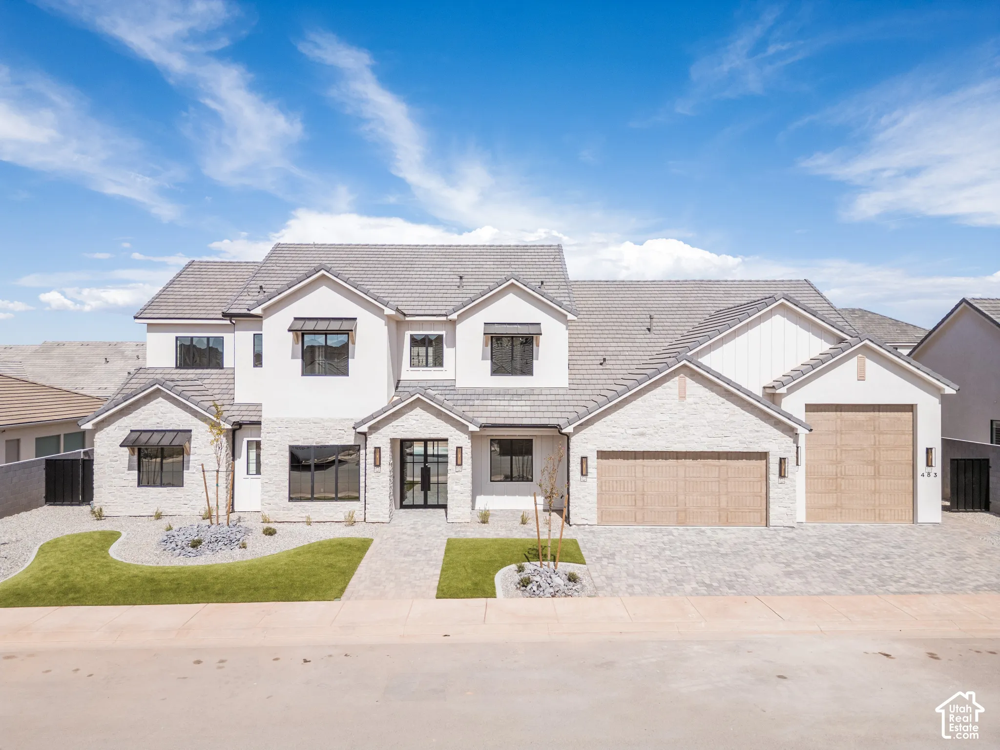 Modern exterior featuring light-colored stone and stucco, a paver driveway, an attached multi-car garage with wood-finish doors, and a tiled roof
