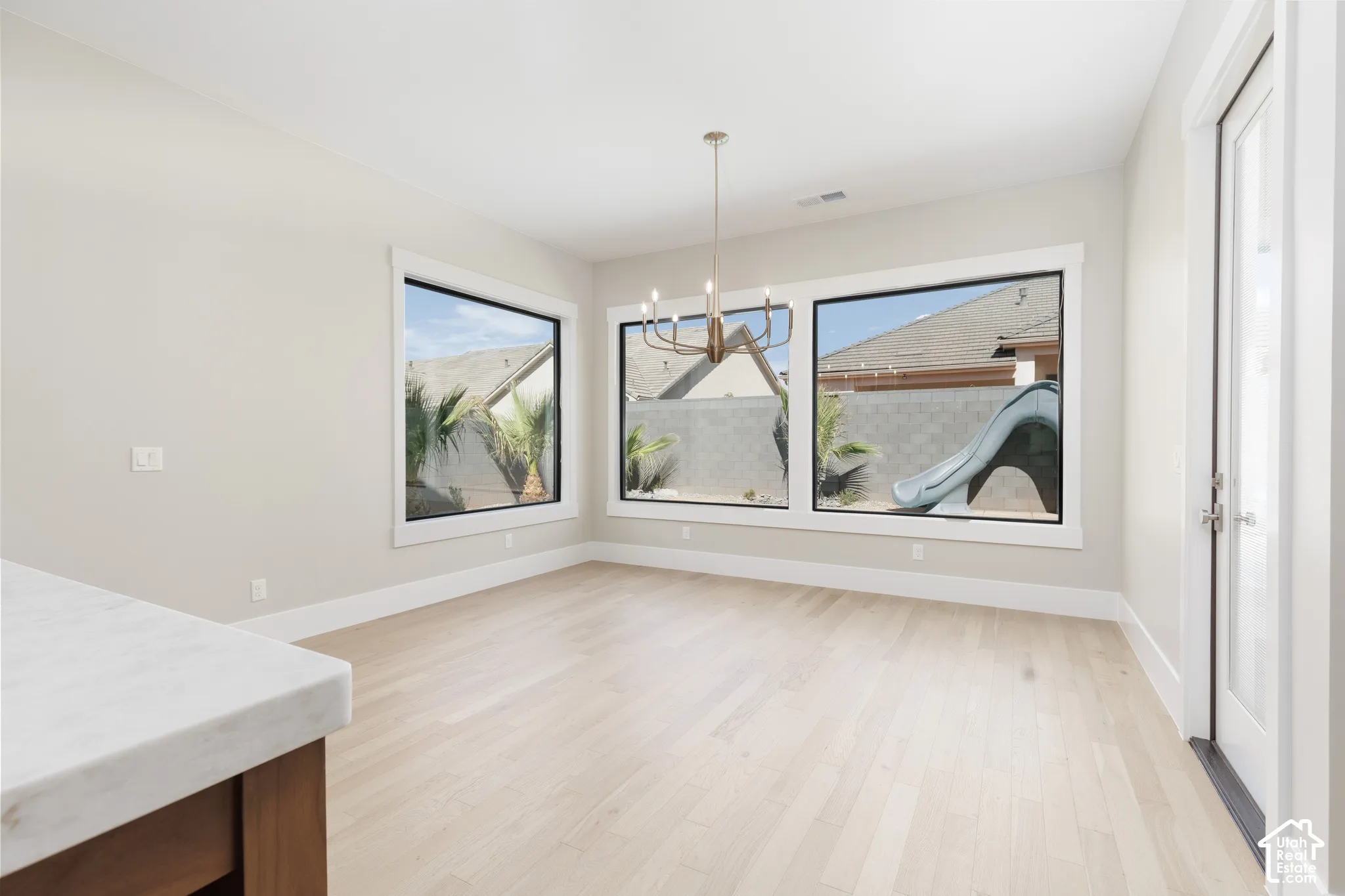 Spacious room with large windows, light wood-finish flooring, and a contemporary chandelier