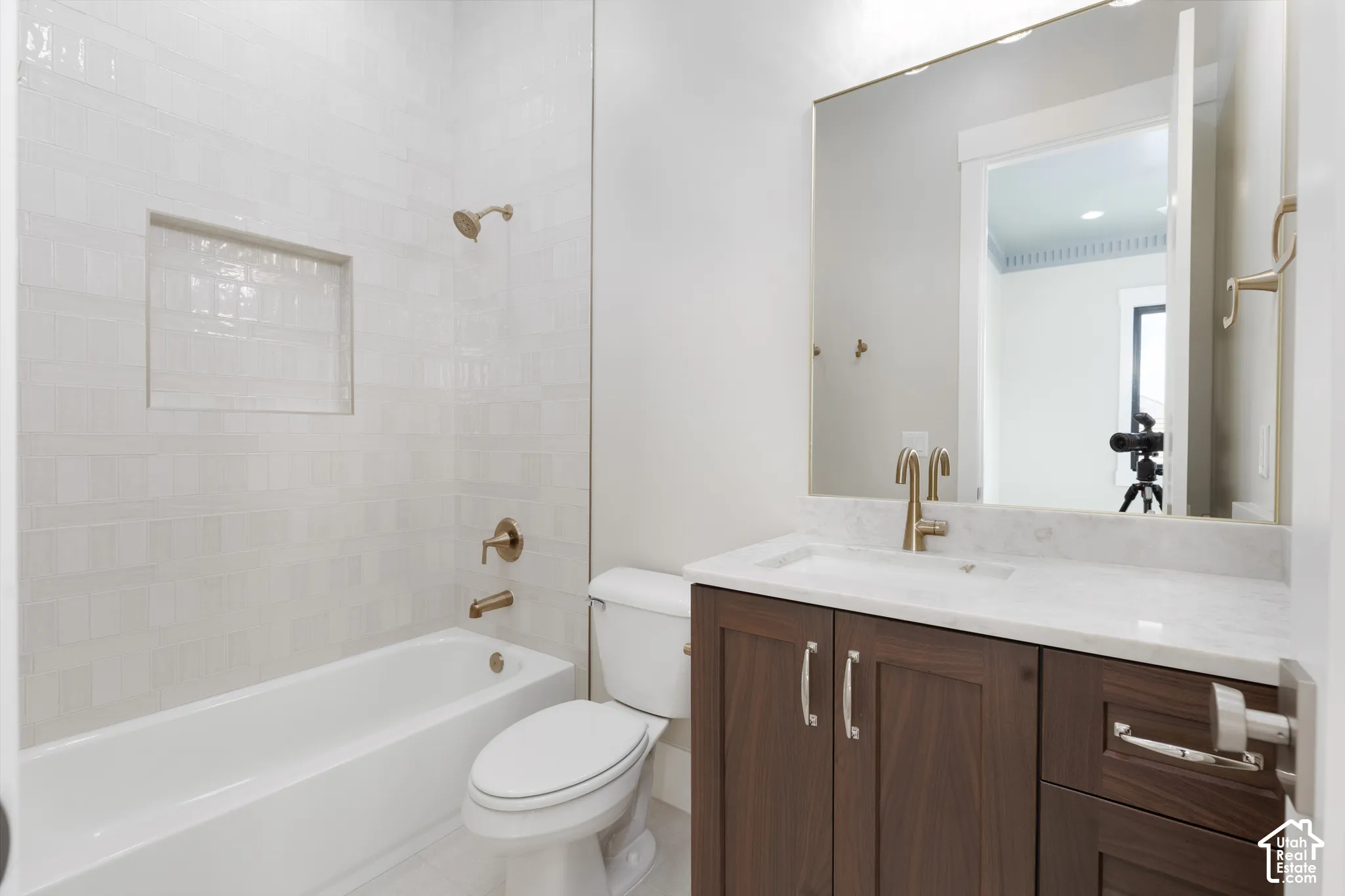 Bathroom featuring a white subway tile tub surround with recessed niche, a built-in bathtub, a wood-finish vanity with a white countertop, and a large wall-mounted mirror