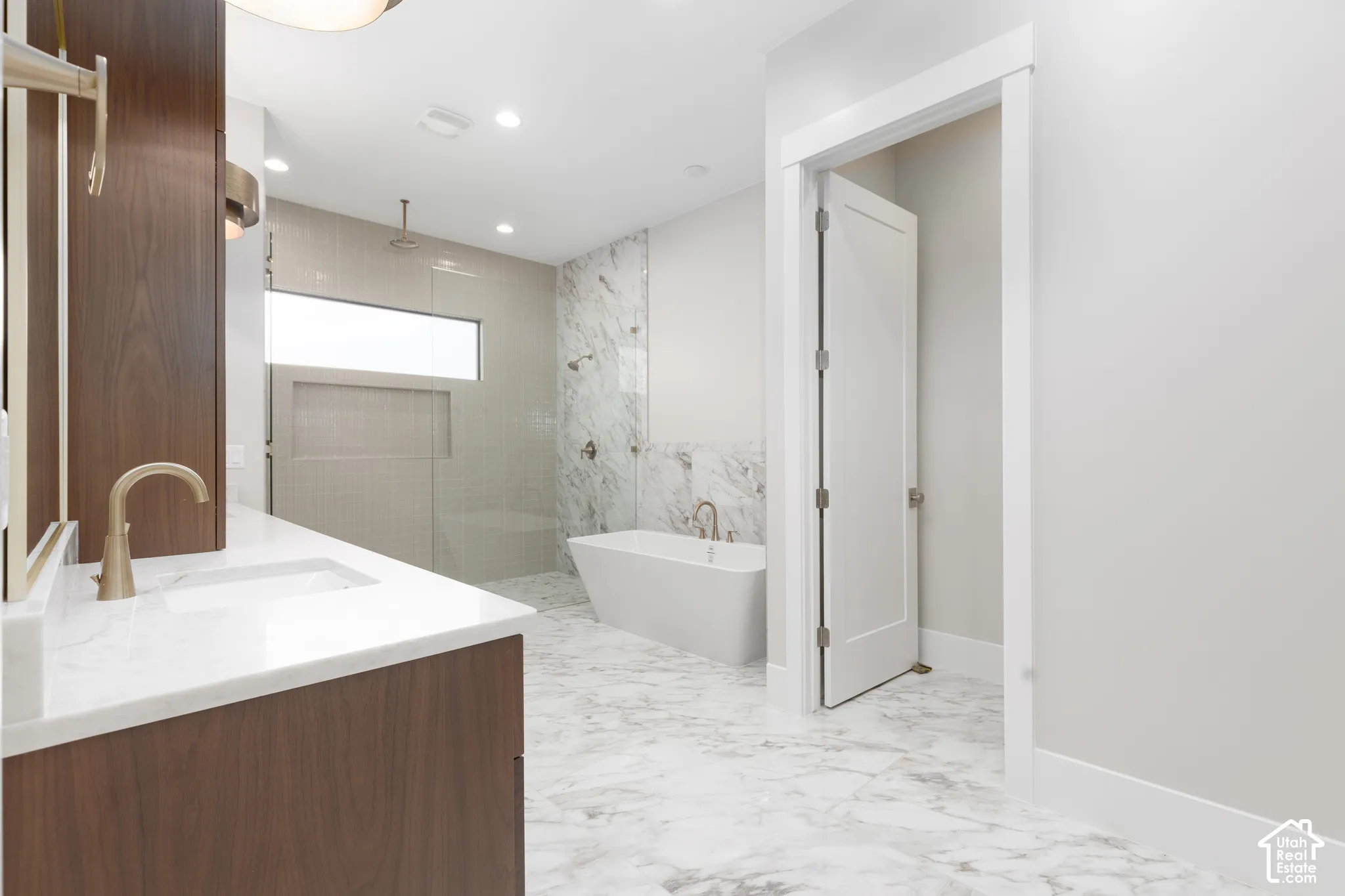 Spacious bathroom featuring a freestanding tub, glass-enclosed shower, wood-finish vanity with an integrated sink, and large format floor tile