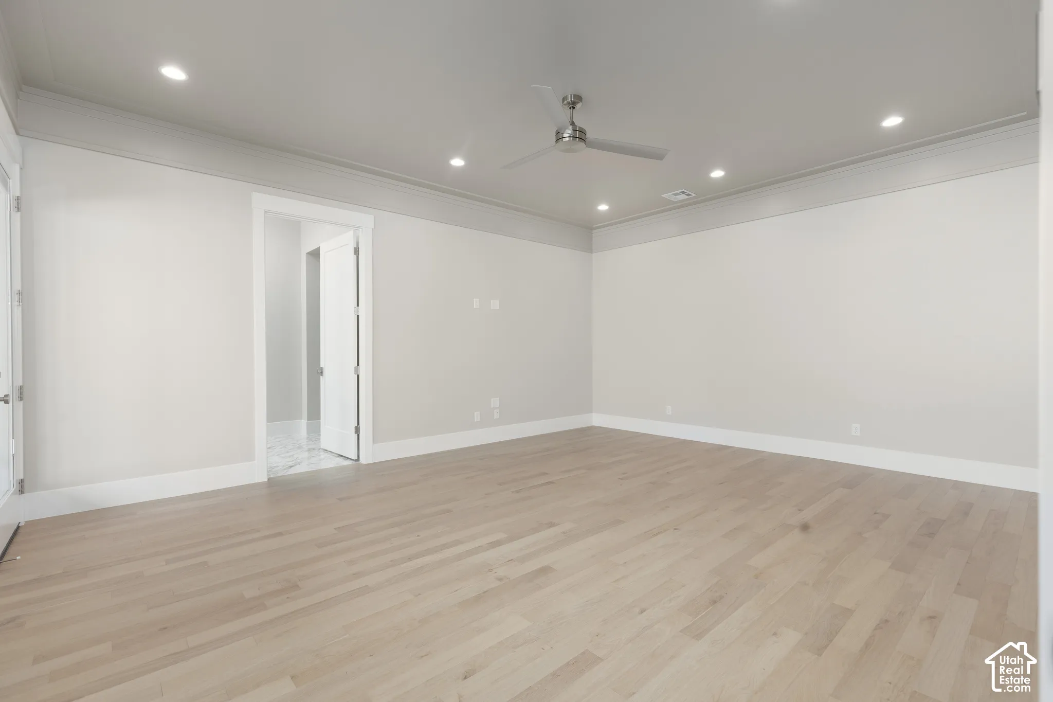 Light wood-finish flooring, recessed lighting, ceiling fan, crown molding, and white trim throughout