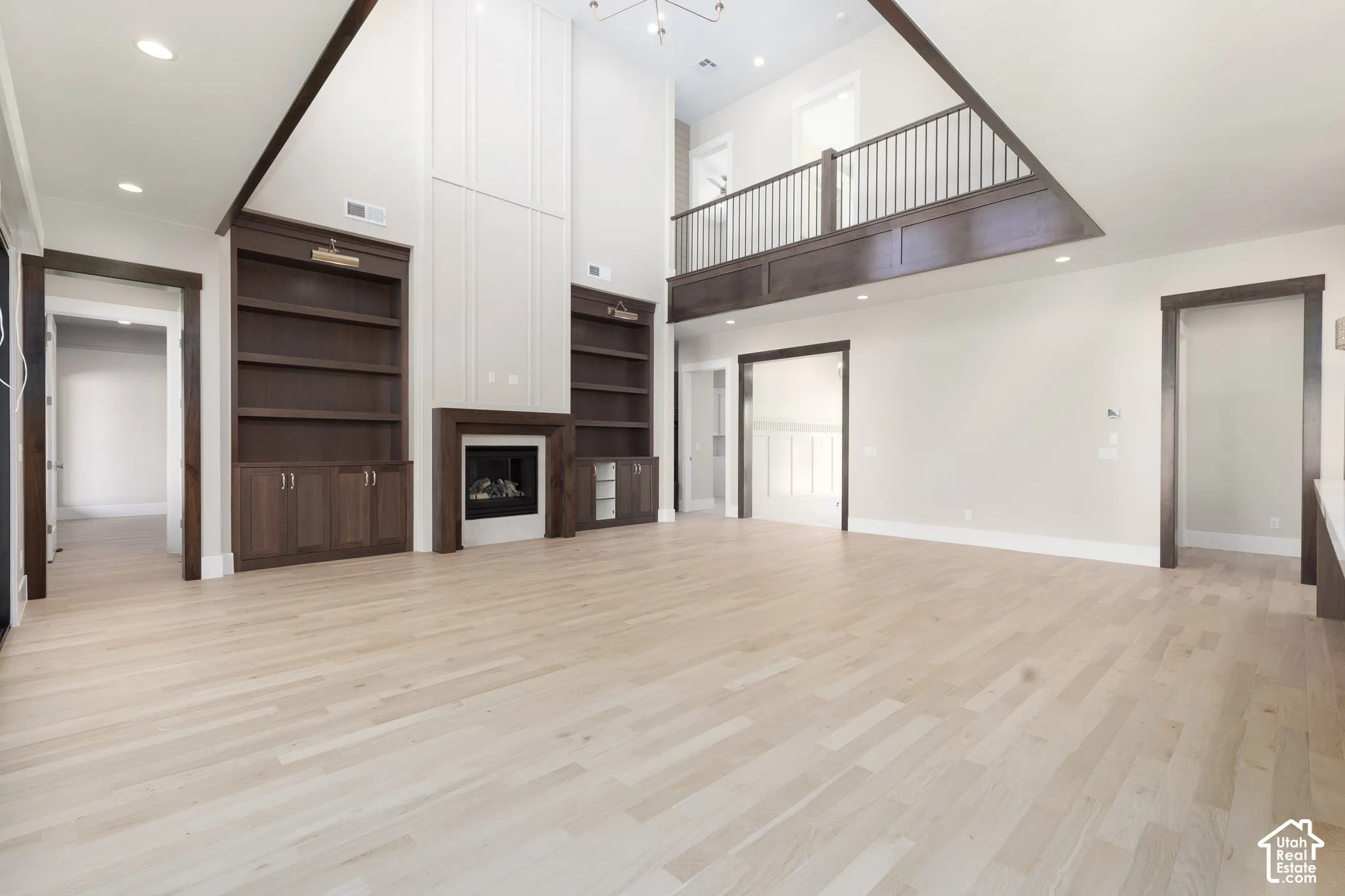 Vaulted ceiling great room with wood-finish flooring, a fireplace, custom built-in shelving, and an upper-level balcony