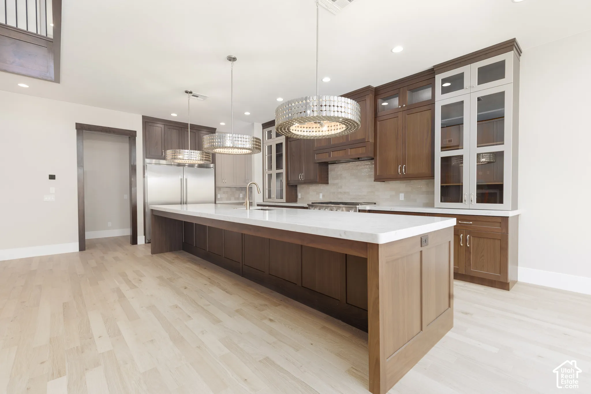 Spacious kitchen featuring a large central island with a light-toned countertop, stainless steel appliances, dark wood-finish cabinetry, and light wood-finish flooring