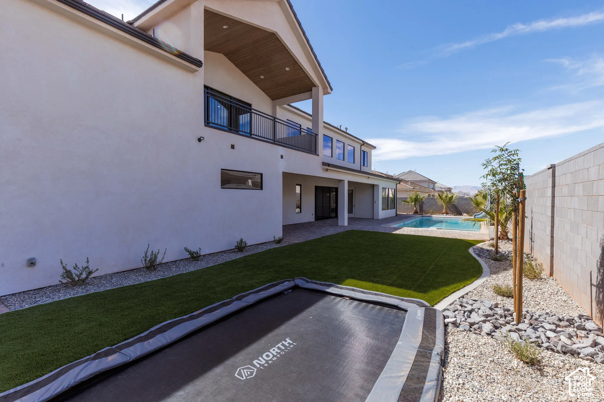 Rear exterior with a second-story balcony, artificial turf, an in-ground swimming pool, and gravel landscaping