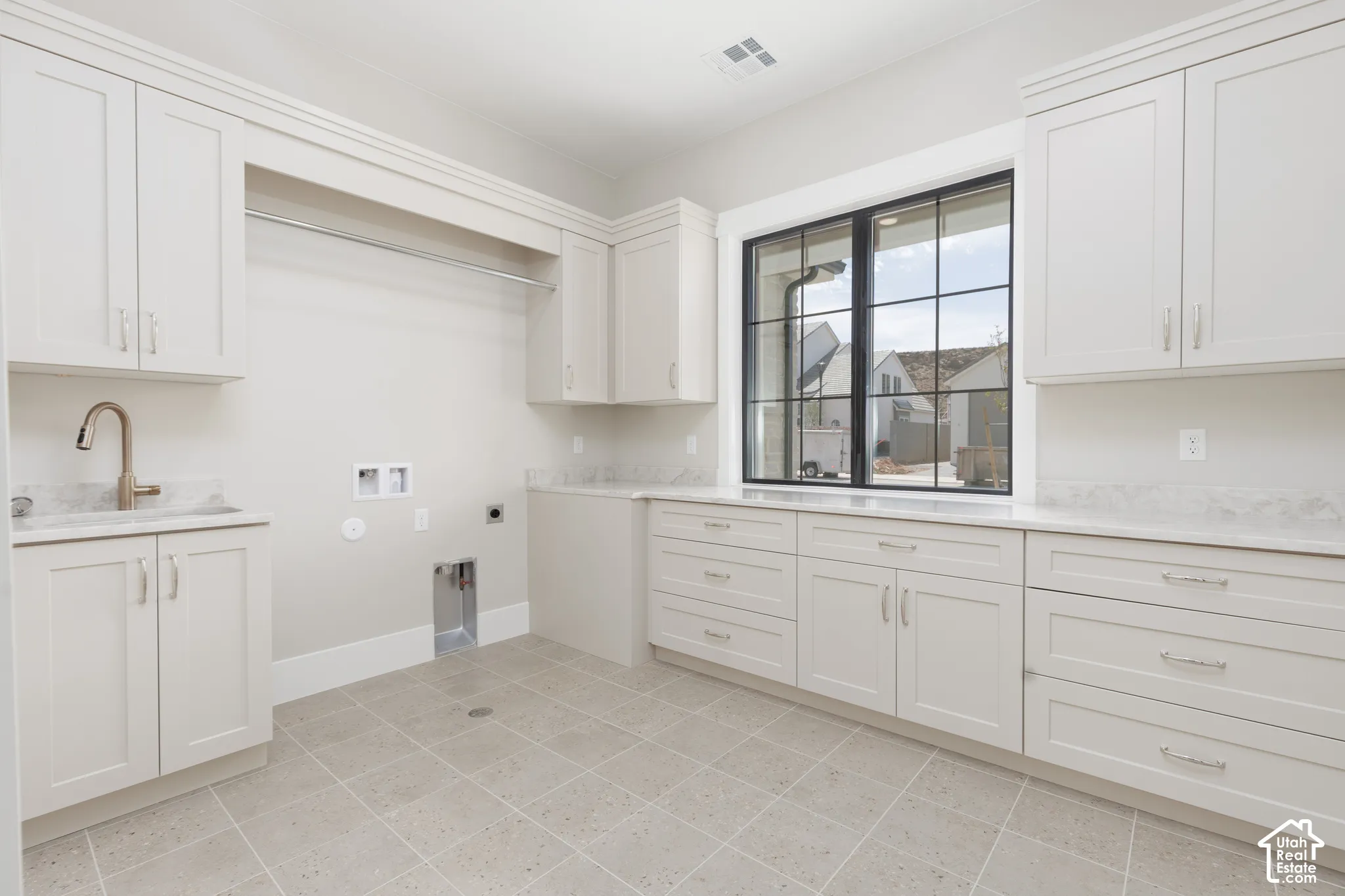 Laundry room featuring extensive white cabinetry, light-toned countertops, a stainless steel sink with a gooseneck faucet, a built-in hanging rod, and a large grid-pattern window