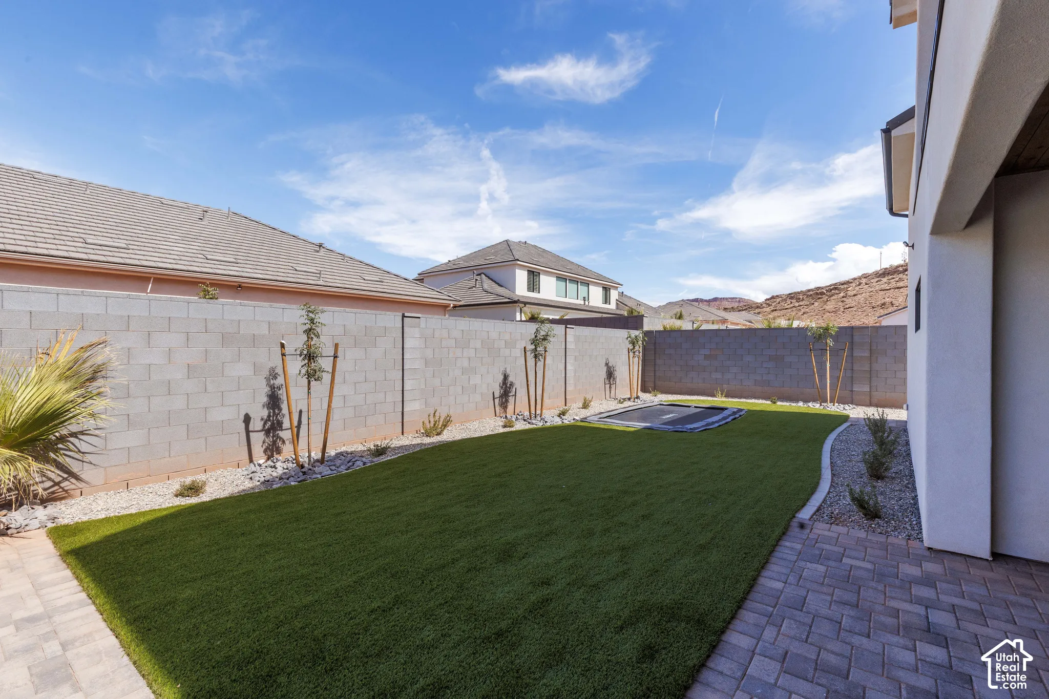 Expansive backyard featuring artificial turf, paver pathways, mature landscaping, and block wall fencing