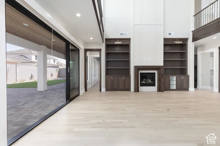 Hardwood-style flooring, gas fireplace with wood surround, built-in shelving and cabinetry, tall ceilings, and expansive sliding glass doors