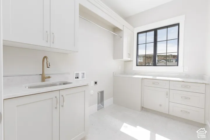 White cabinetry with brushed nickel hardware, light-toned countertops, and a utility sink with a tall brass-finish faucet
