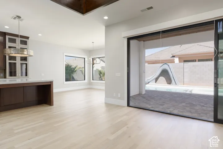 Wide plank wood-finish flooring, recessed lighting, and a modern chandelier illuminate the expansive living area