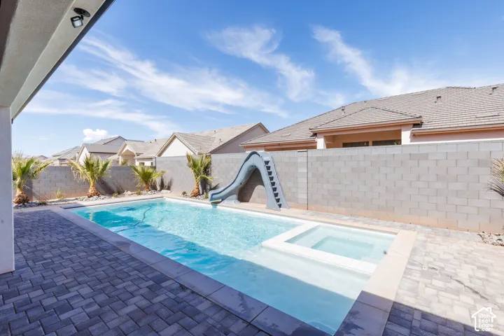 Outdoor swimming pool with an integrated spa, a built-in slide, and paver decking