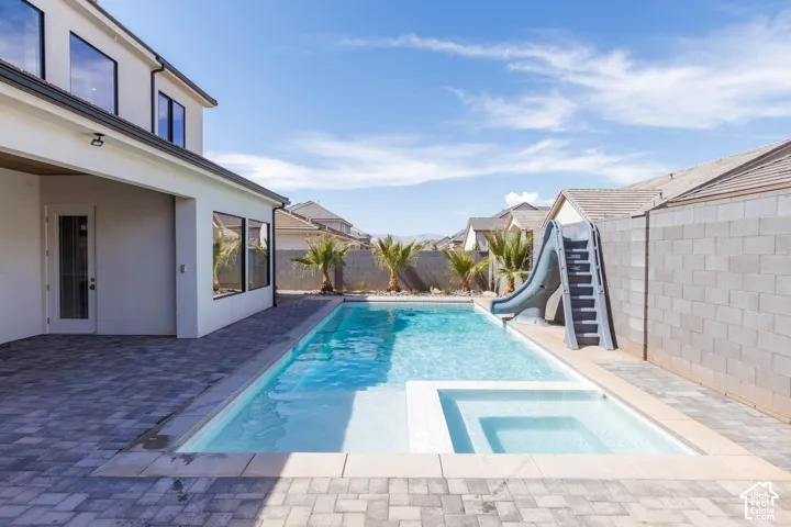 Resort-style backyard oasis featuring a resort-style swimming pool with integrated spa, travertine-look paved decking, a water slide, and mature tropical landscaping
