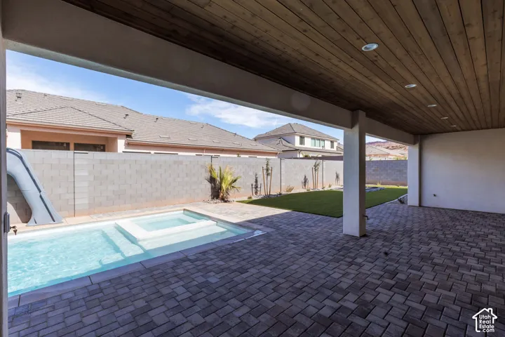 Covered patio with wood-finish ceiling and recessed lighting, paver flooring, integrated pool and spa, and a grass lawn area