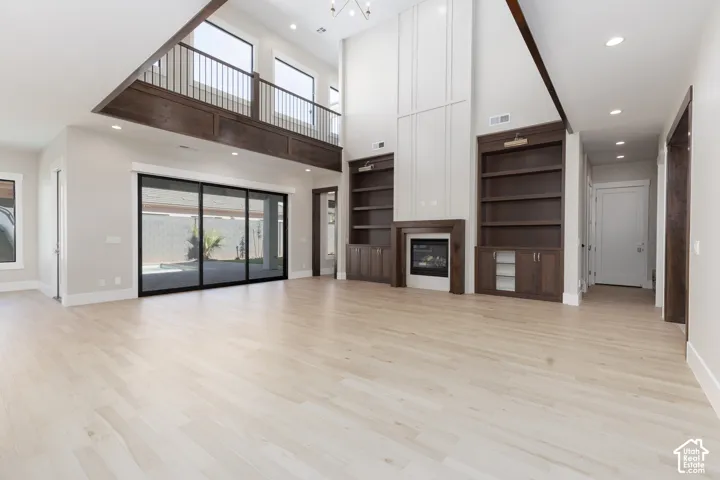Two-story ceiling, light wood-finish flooring, built-in shelving, fireplace with mantel, and large sliding glass doors