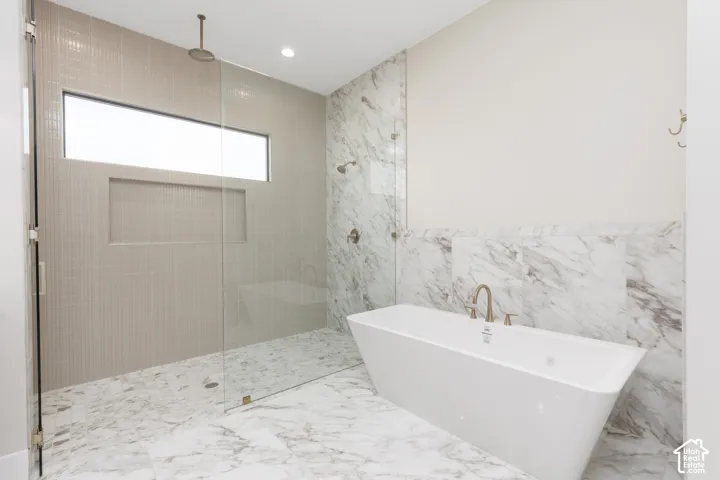 Freestanding soaking tub with a wall-mounted faucet, glass-enclosed shower with a rainfall shower head, and full tile flooring