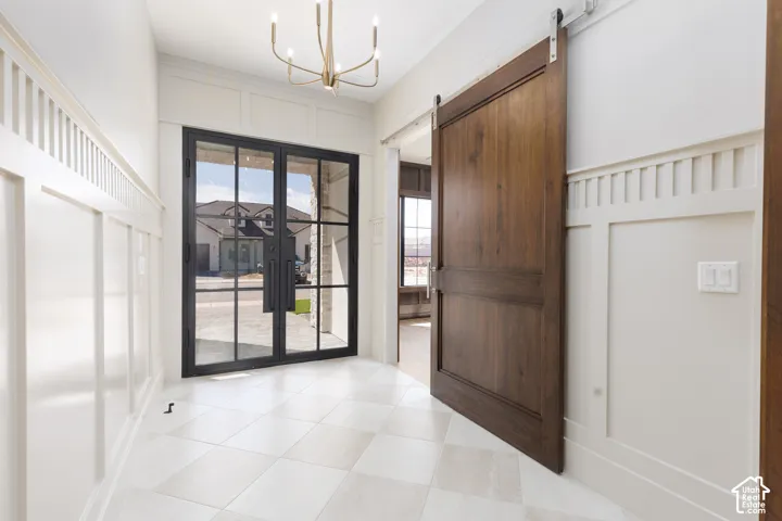 Entryway featuring board and batten wall paneling, large format tile flooring, a modern chandelier, and a dark wood barn door