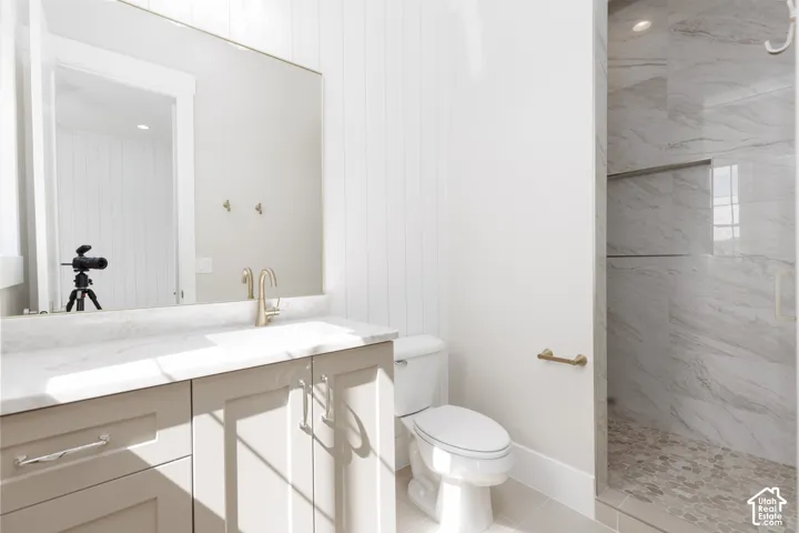 Bathroom featuring a single vanity with light-toned cabinetry, a spacious mirror, and a walk-in shower with tiled walls and a mosaic floor