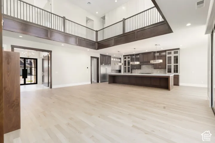 Two-story great room featuring light wood-finish flooring, a kitchen with dark wood cabinetry, a central island, and stainless steel appliances