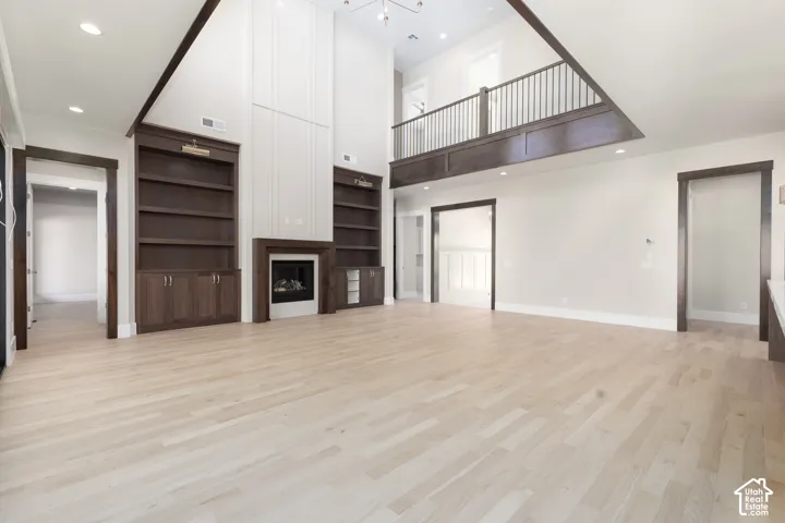 Vaulted ceiling great room with wood-finish flooring, a fireplace, custom built-in shelving, and an upper-level balcony