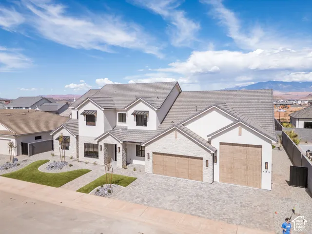 Contemporary residence featuring a two-car garage, stone and stucco exterior, paver driveway, and manicured front landscaping