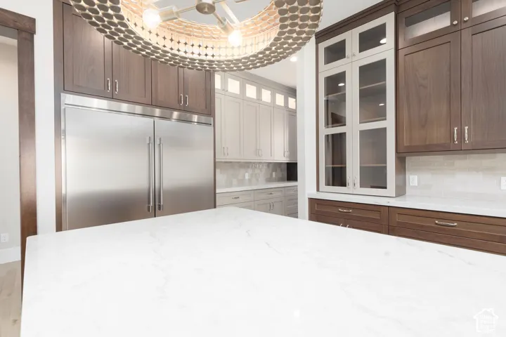 Spacious kitchen island with a white stone countertop, integrated stainless steel refrigerator, dark wood-finish cabinetry, and glass-front upper cabinets