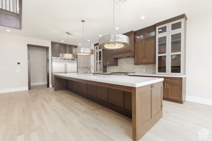 Spacious kitchen featuring a large central island with a light-toned countertop, stainless steel appliances, dark wood-finish cabinetry, and light wood-finish flooring