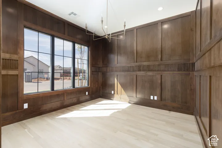 Light wood-finish flooring, dark wood wall paneling, large grid-pane windows, and a modern linear chandelier
