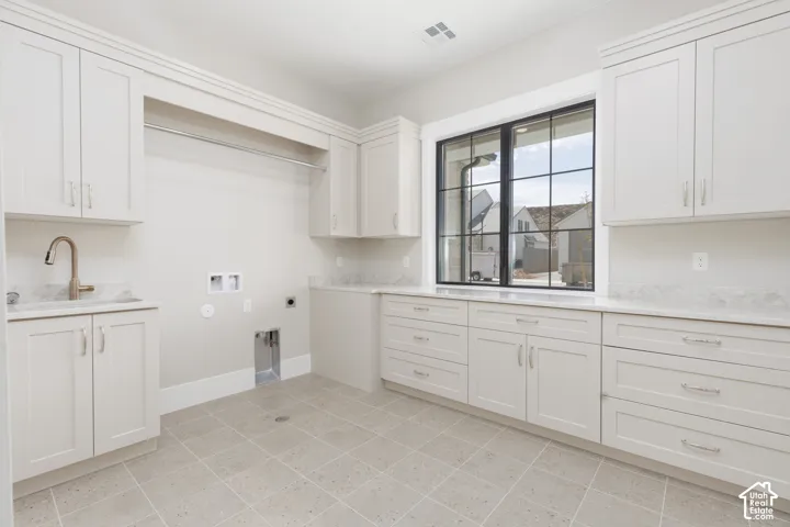 Laundry room featuring extensive white cabinetry, light-toned countertops, a stainless steel sink with a gooseneck faucet, a built-in hanging rod, and a large grid-pattern window