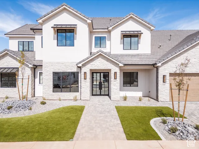 Modern exterior featuring a light-toned stone and stucco facade, a paver walkway, and a dark metal-framed double entry door