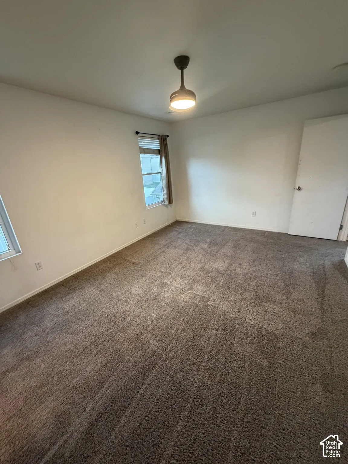 Neutral tone wall paint, textured carpet flooring, window with blinds, and a flush-mount ceiling light fixture