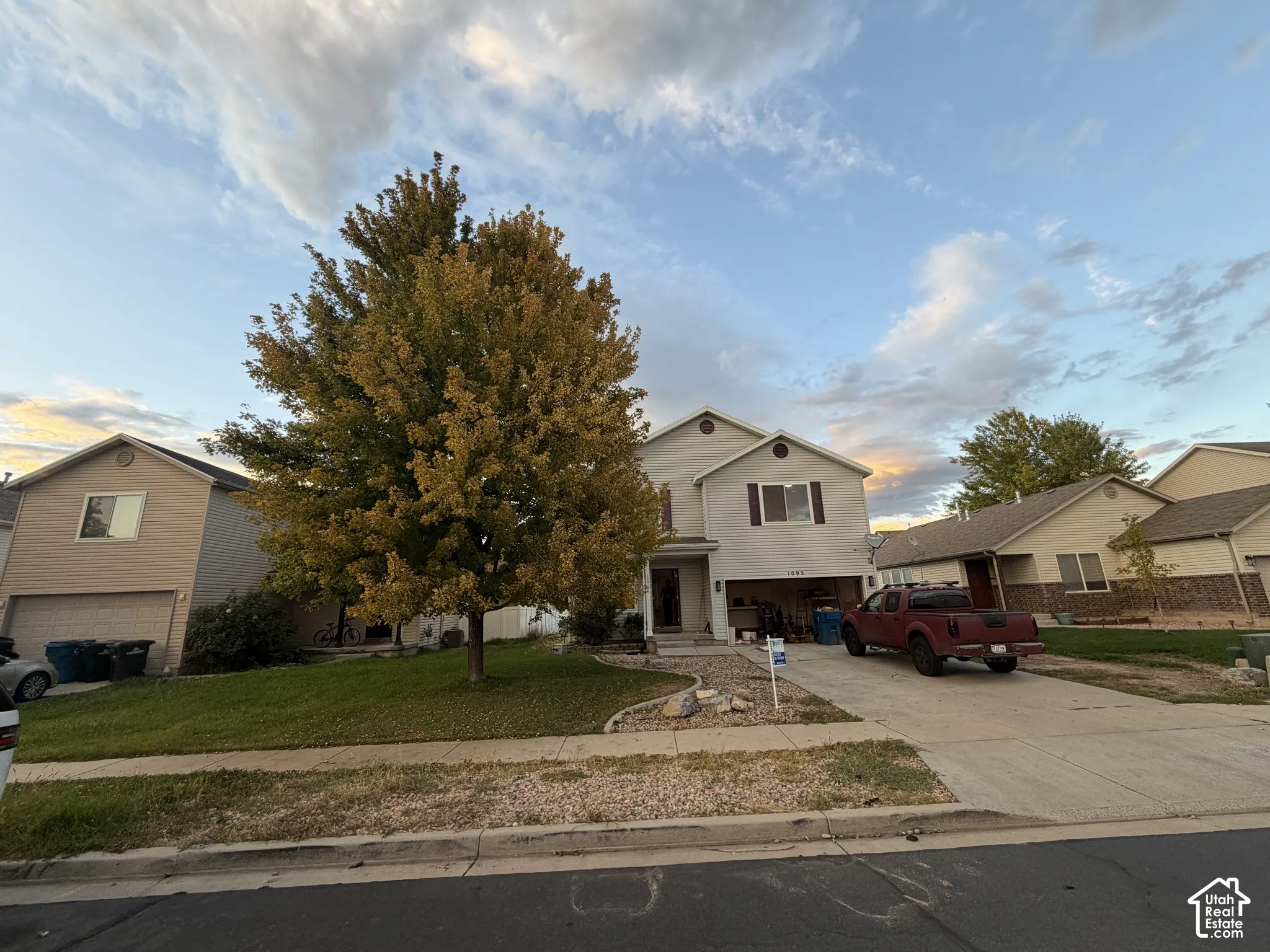 Two-story residence with a two-car garage, front yard landscaping, and a beautiful mature tree