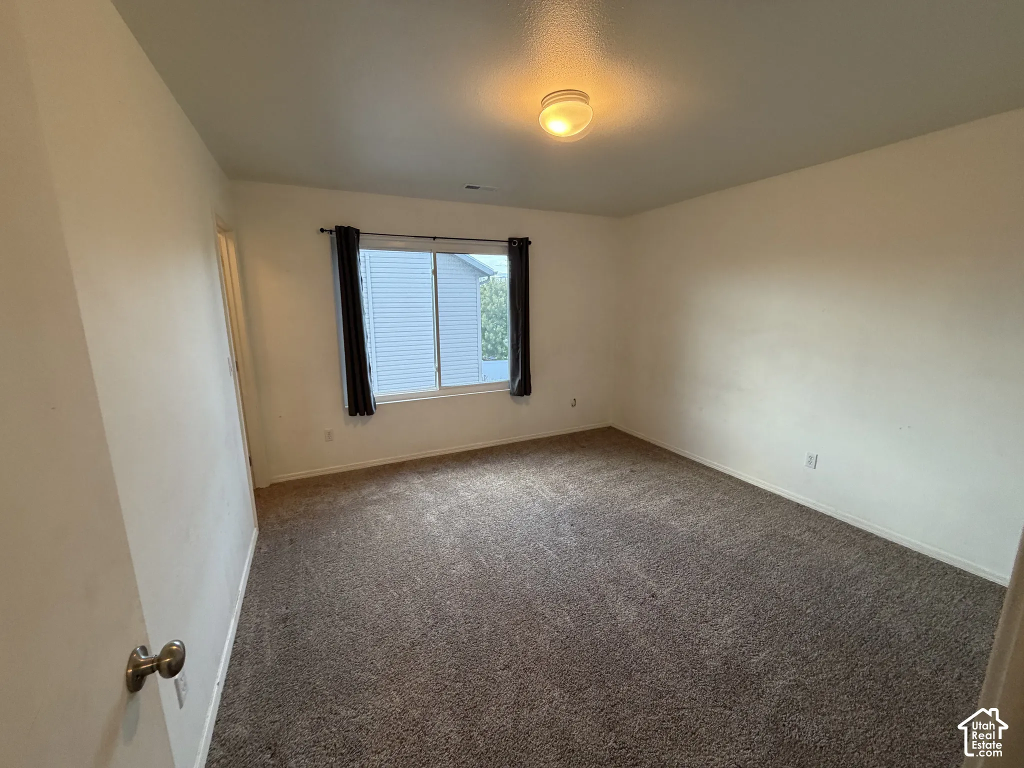 Spacious room featuring neutral carpeting, white walls, a large window, and an overhead light fixture