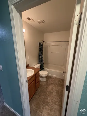 Bathroom featuring wood-finish vanity with integrated sink, white toilet, and a white tub with shower