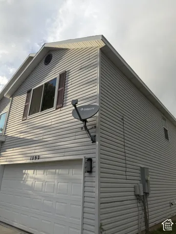 Light-toned siding exterior with a paneled garage door, decorative window shutters, and an exterior wall lantern