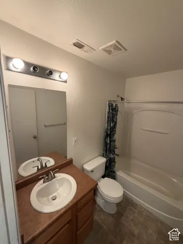 Bathroom featuring a single vanity with wood-finish cabinetry, an oval sink, a brushed nickel faucet, and a shower-tub combination