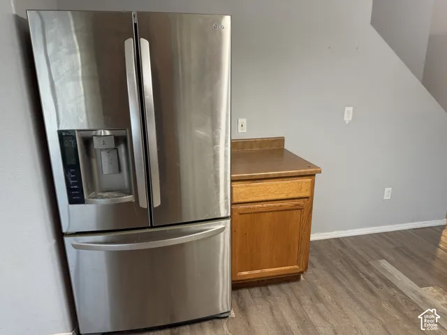 Stainless steel refrigerator with French doors and an exterior ice/water dispenser, wood-finish flooring, and a base cabinet with a countertop