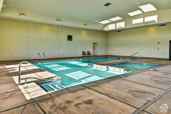 Indoor swimming pool with an integrated spa, durable concrete decking, and overhead skylights