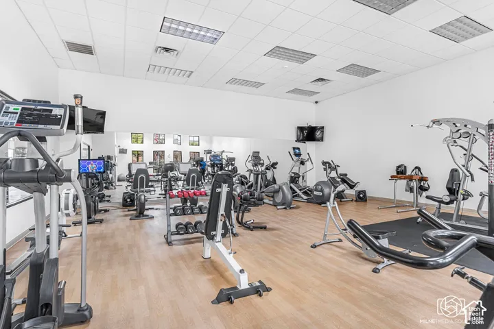 State-of-the-art fitness facility featuring an extensive array of cardio and strength-training equipment, wood-finish flooring throughout, bright overhead lighting with recessed fixtures, and ample open space for functional training and movement