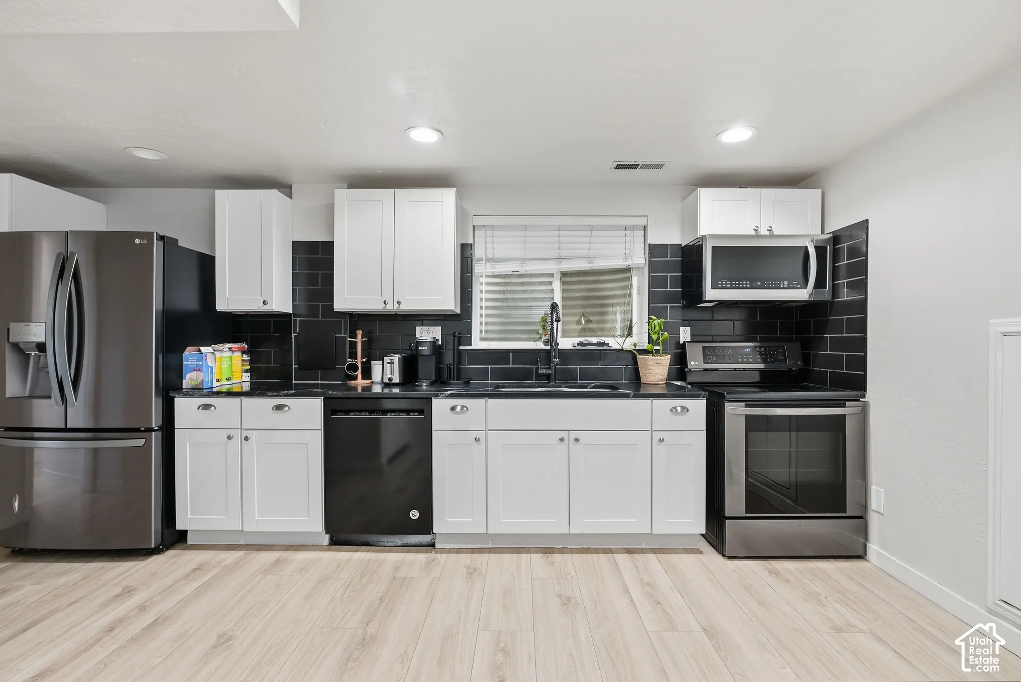 Kitchen featuring white cabinetry, black subway tile backsplash, dark countertops, recessed lighting, and light wood-finish flooring