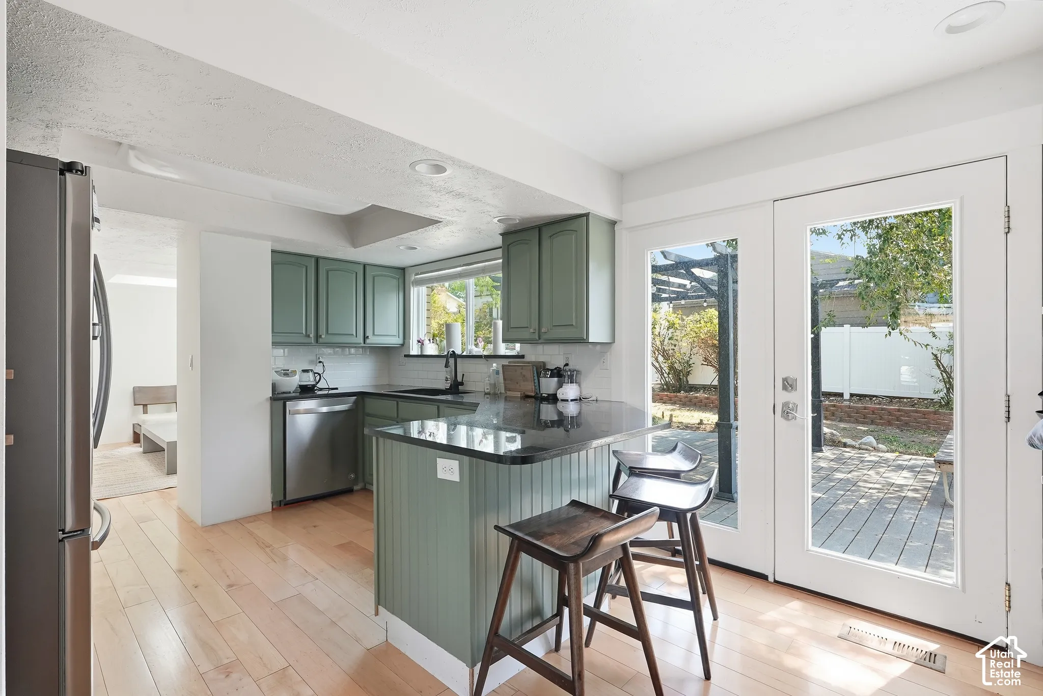 Kitchen featuring light wood-finish flooring, green cabinetry, a central island with a dark countertop, stainless steel appliances, and French doors leading to an outdoor patio