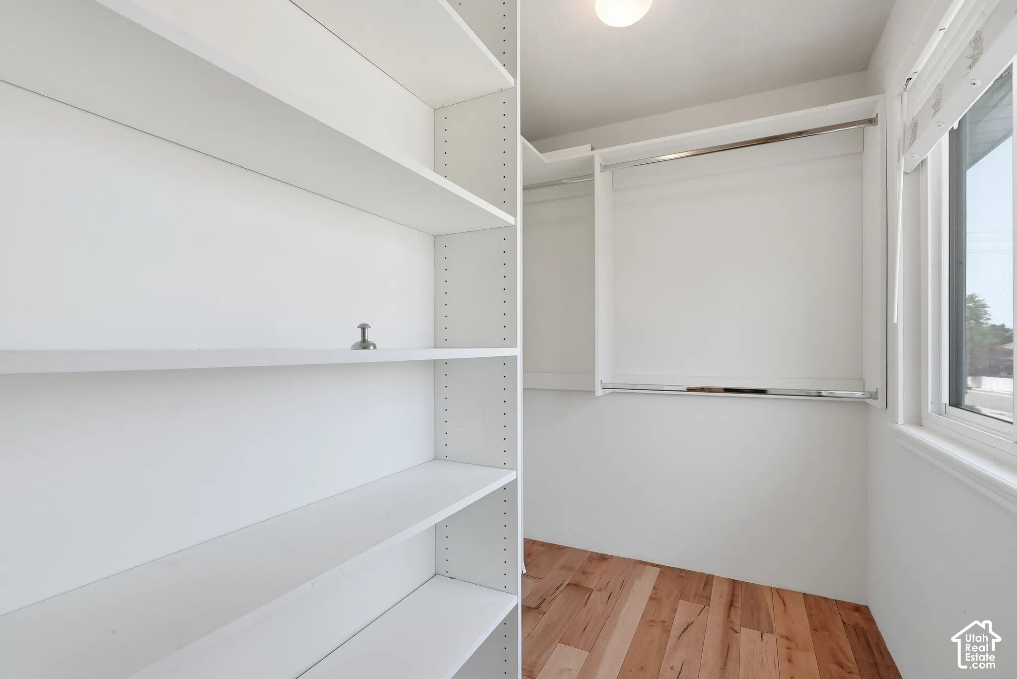 Adjustable white shelving, wood-finish flooring, recessed lighting, and a window with roller shades