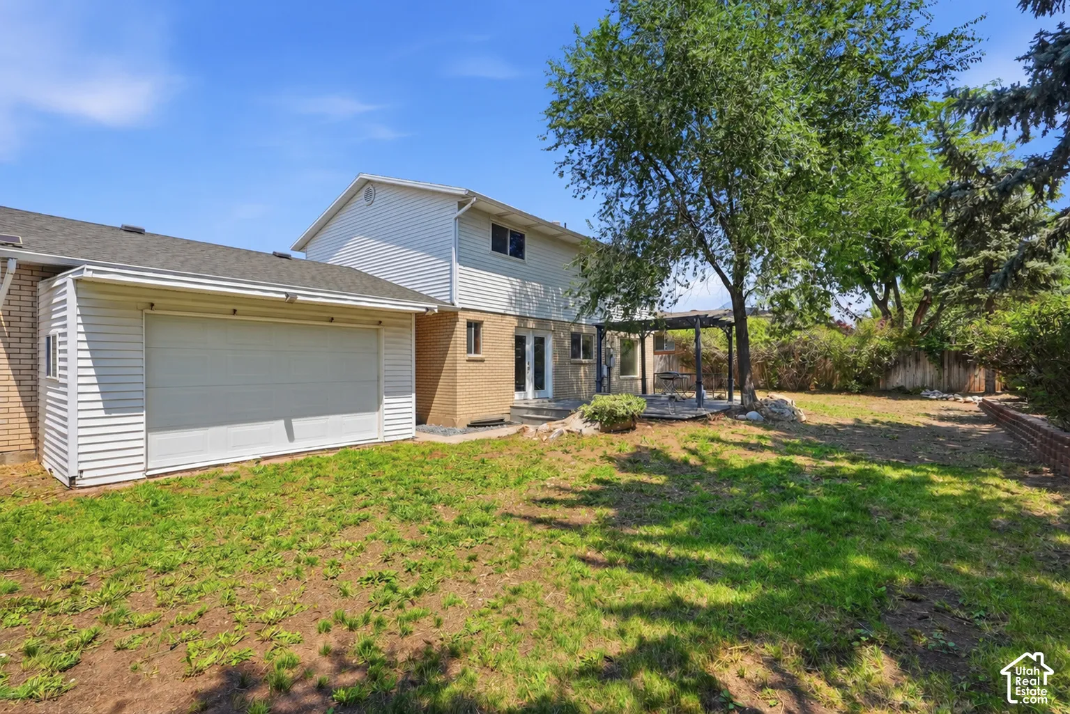 Expansive backyard featuring a pergola, mature trees, and a brick retaining wall
