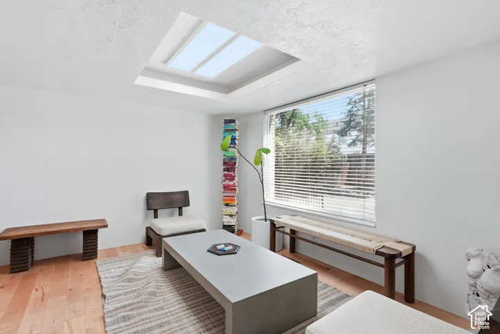 Hardwood flooring, recessed ceiling with skylight, large window with blinds, and white walls