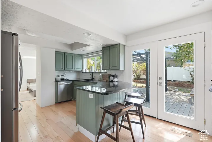 Kitchen featuring light wood-finish flooring, green cabinetry, a central island with a dark countertop, stainless steel appliances, and French doors leading to an outdoor patio