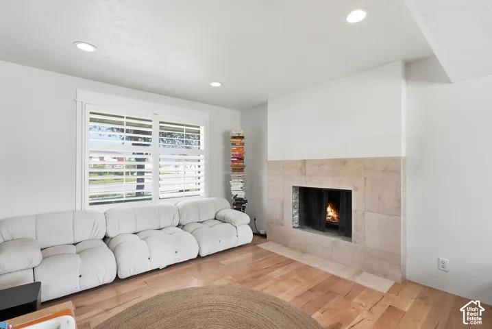 Stone-faced fireplace with hearth, recessed lighting, wood-finish flooring, and window with plantation shutters