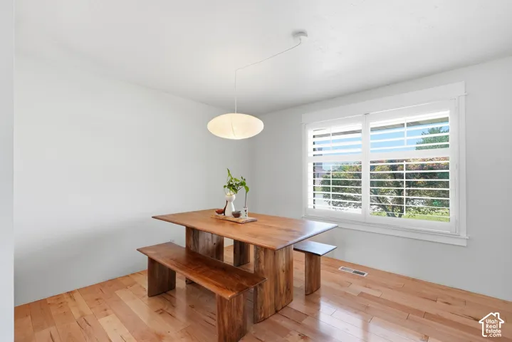 Light wood-finish flooring, white walls, large window with white plantation shutters, and a modern pendant light fixture