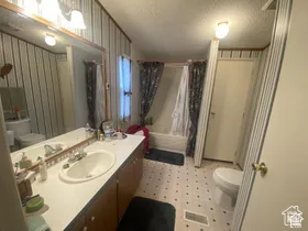 Vanity with two integrated sinks and chrome fixtures, wall-mounted light fixture, full-width mirror, and a built-in tub with shower