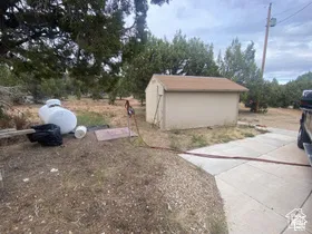 Outdoor storage shed with a brown shingle roof, a concrete driveway, and a white propane tank