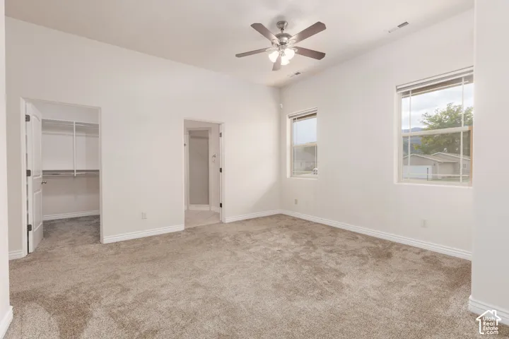 Spacious primary bedroom featuring neutral carpeting, a ceiling fan with light, and multiple windows
